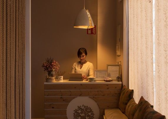 Recepción del centro iluminada por una lámpara cálida, con Gema tras el mostrador de madera.