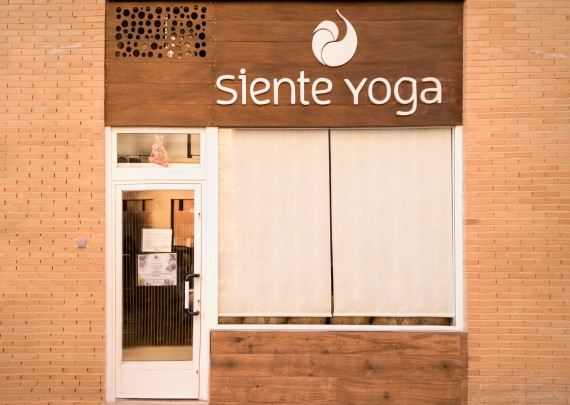 Fachada del centro con el letrero de madera «siente yoga» y el isotipo en espiral.